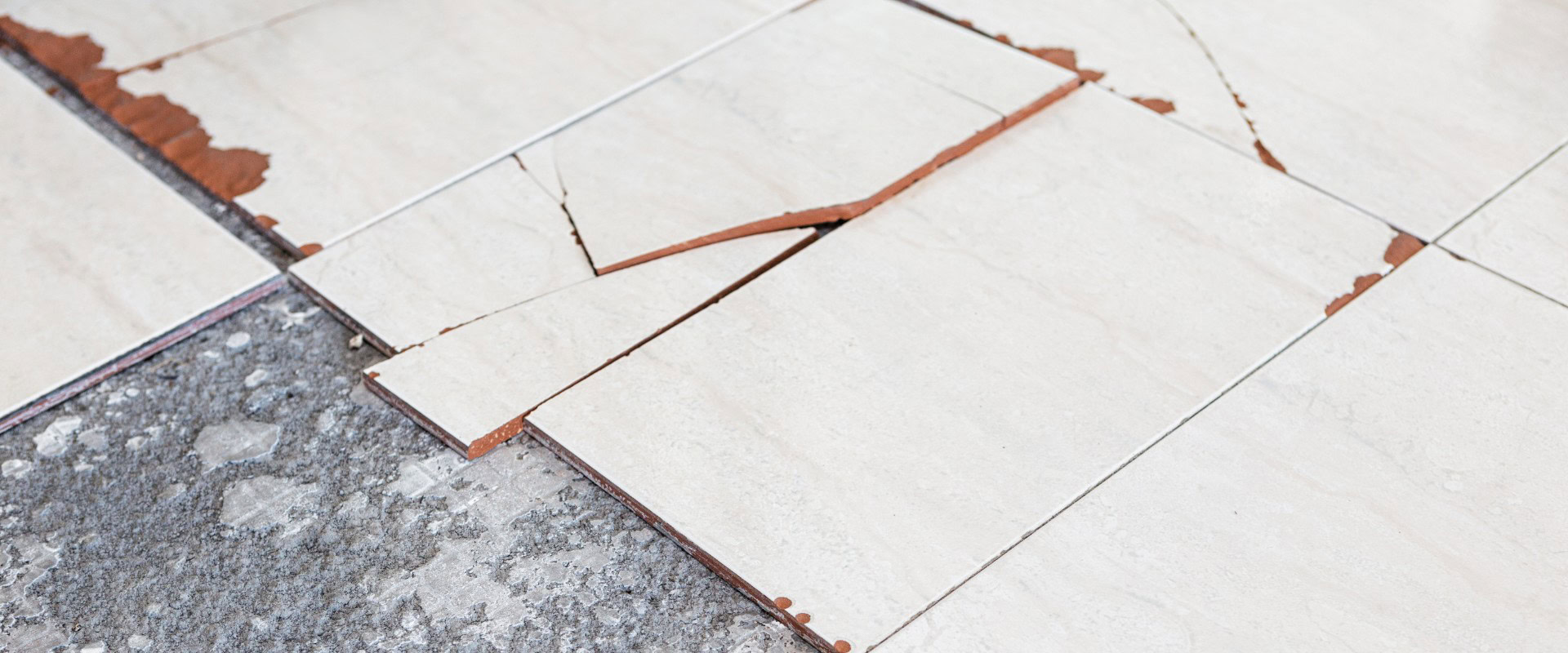 Cracked floor tiles with exposed adhesive and substrate in older building, potential asbestos-containing legacy materials