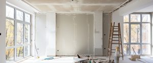 Interior of an unfinished room with large windows, a ladder, and construction materials on the floor.