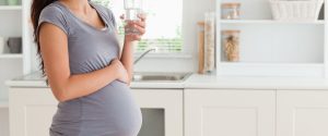 A pregnant woman drinking water in a kitchen